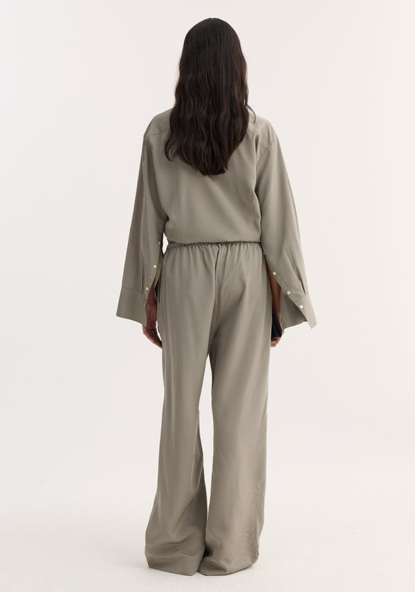 Back view of person in Relaxed fit trousers, light grey stripe, with wide legs and drawstring waistband, paired with a matching pin-stripe shirt, holding a black accessory.