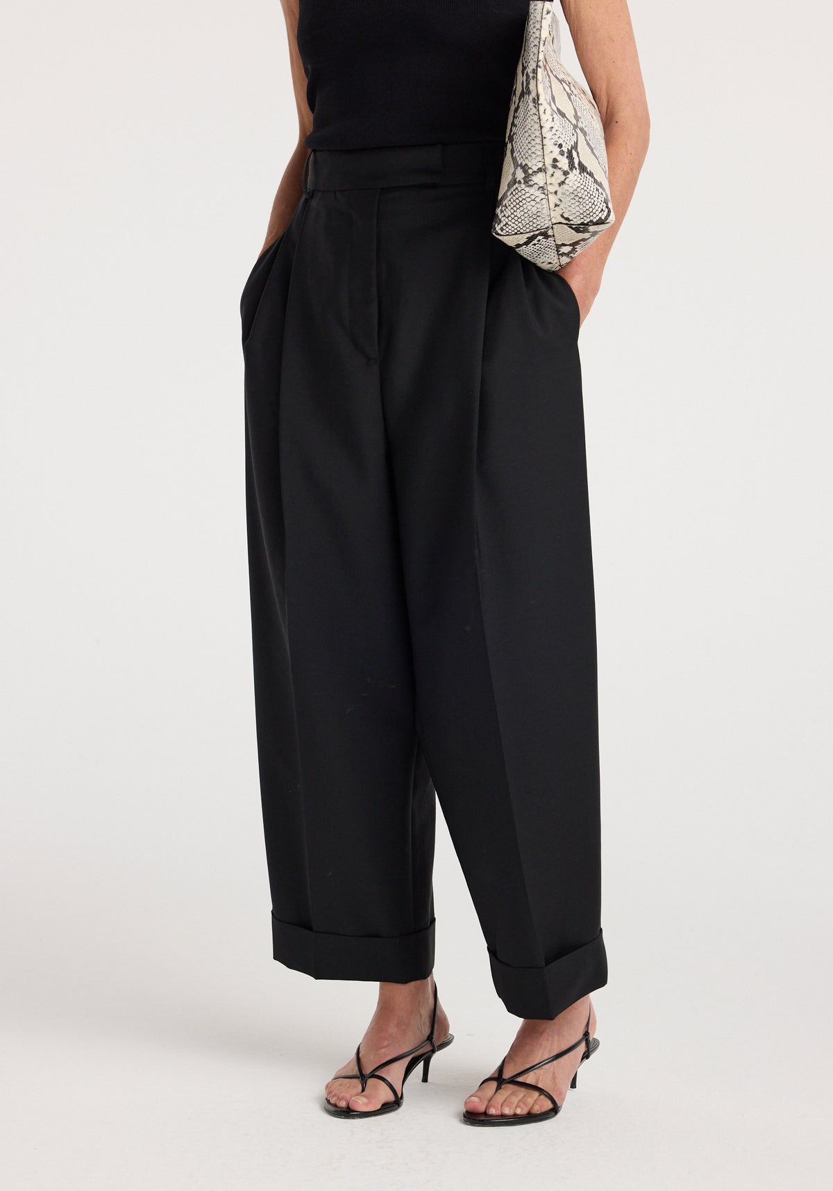 High-waist turn-up trousers | black worn with folded cuffs, side pockets, strappy sandals, and a snakeskin shoulder bag.
