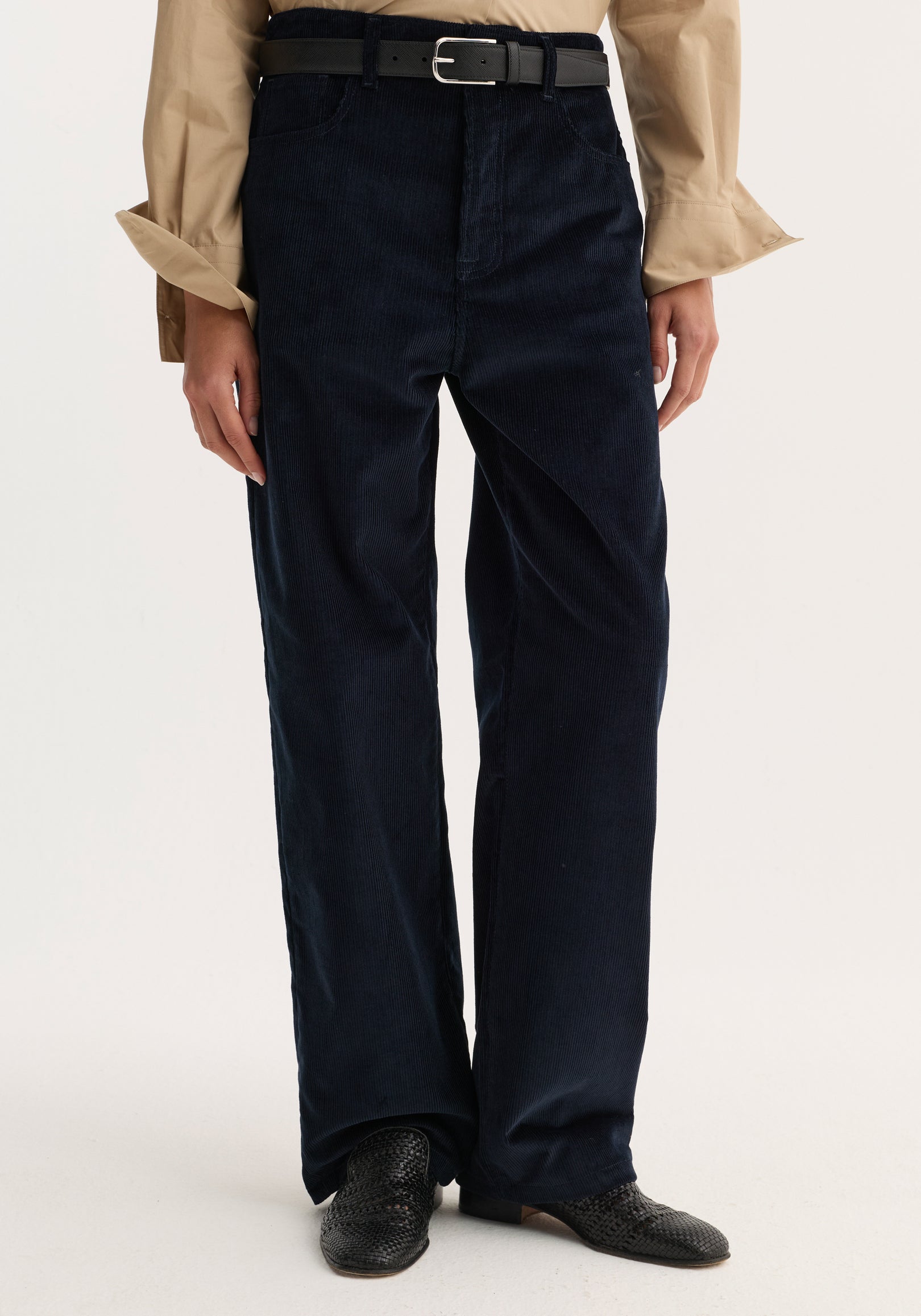Model wearing Relaxed corduroy trousers | night with a straight-leg fit, black belt, beige shirt, and black woven slip-on shoes.