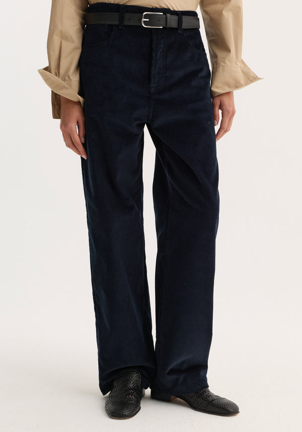 Model wearing Relaxed corduroy trousers | night with a straight-leg fit, black belt, beige shirt, and black woven slip-on shoes.