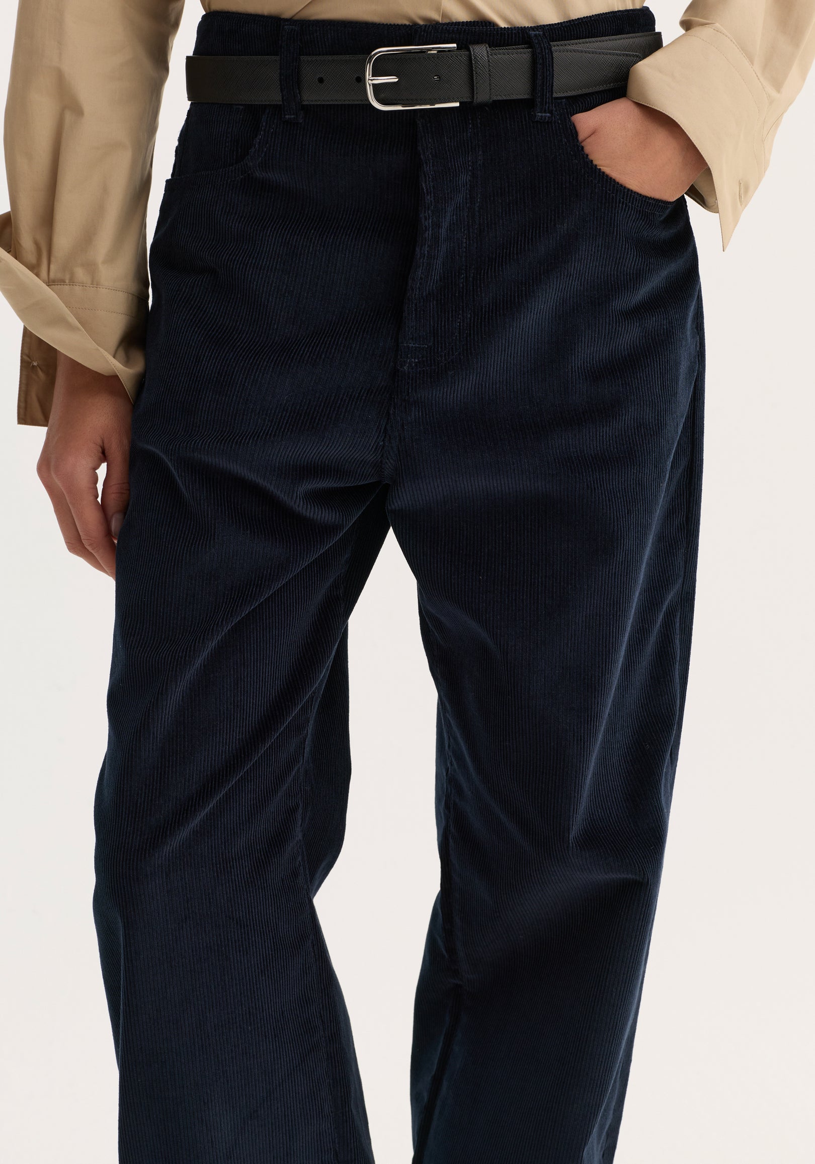 Close-up of Relaxed corduroy trousers | night, featuring navy corduroy, loose leg, denim-style details; worn with a black belt and beige shirt.