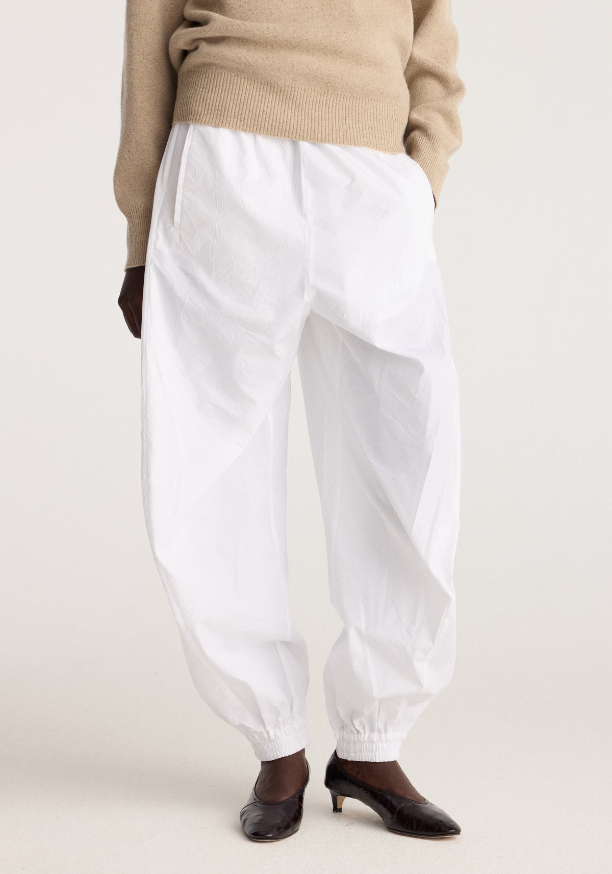 Balloon track pants | optic white shown on a model with a relaxed balloon silhouette elastic cuffs and lightweight crinkled fabric styled with a beige sweater and black flats