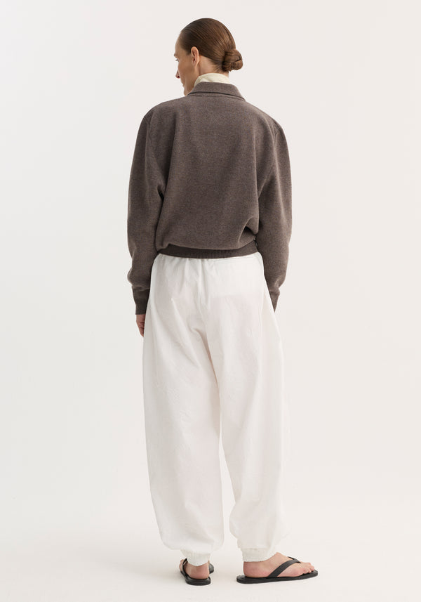 Back view of model in Balloon track pants | optic white, featuring crinkled texture, elastic waistband, voluminous legs, and welt pockets, paired with a muted sweater.