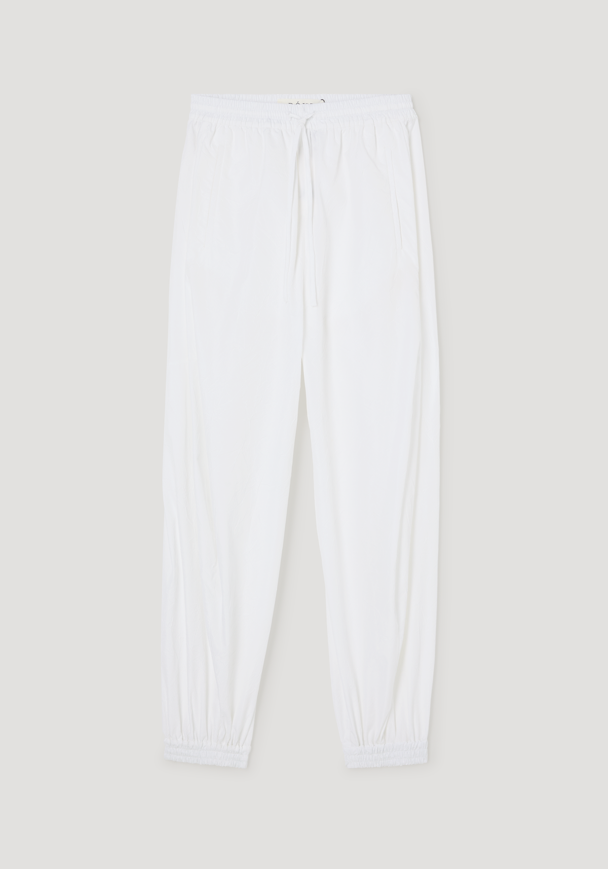 Balloon track pants in optic white with crinkled texture, featuring an elastic waistband, drawstring, welt pockets, and elastic cuffs for a voluminous look.