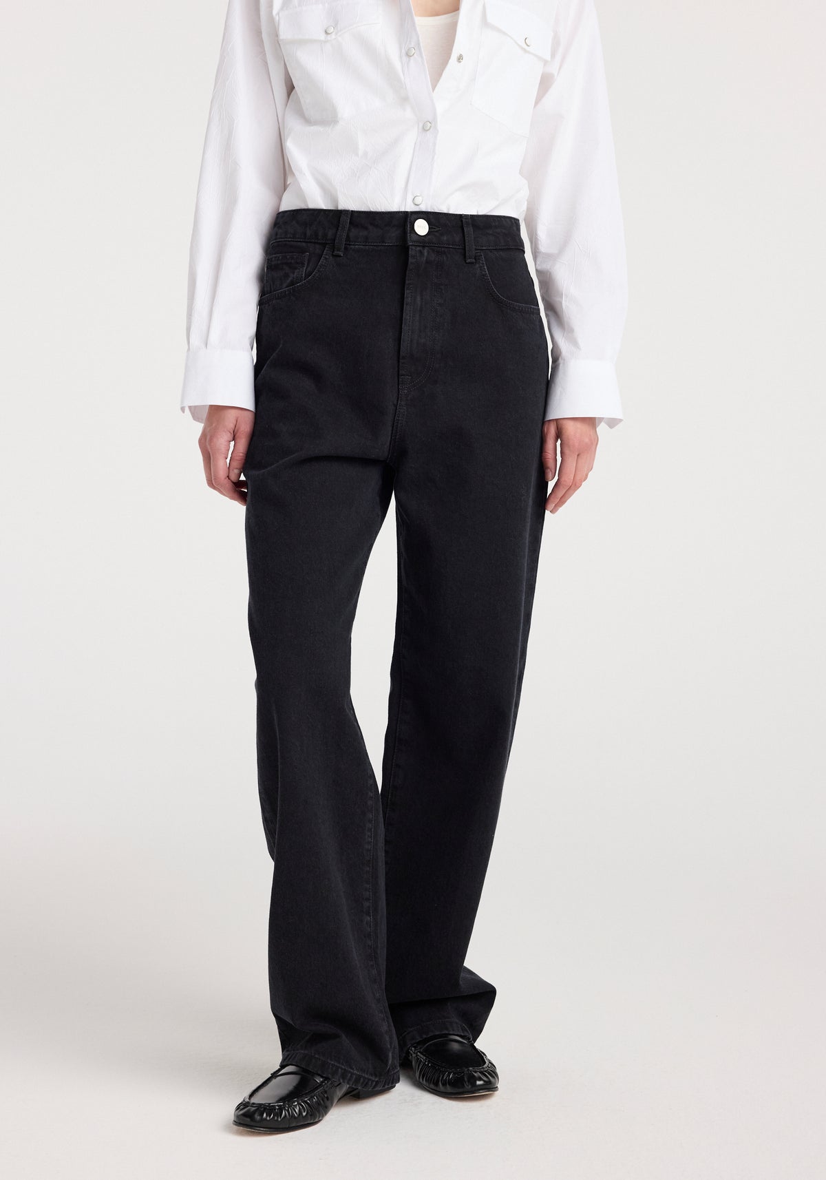 Front view of a person wearing Bruun - Signature baggy denim | black paired with a white button-up shirt and black shoes, showcasing the loose fit and high waist design of the jeans.