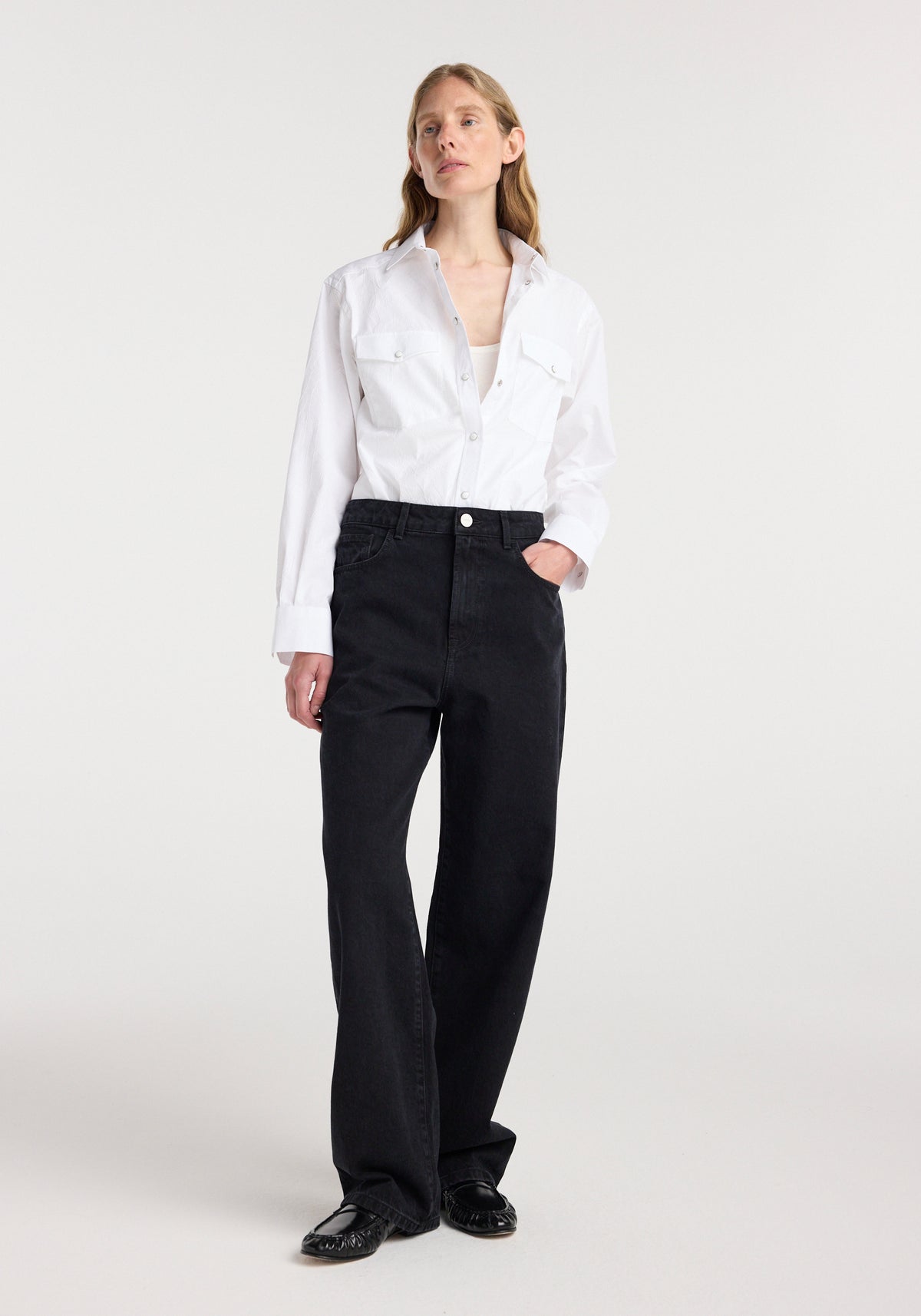 Woman wearing black Bruun - Signature baggy denim | black paired with a white button-up shirt and black shoes, standing against a plain light background.