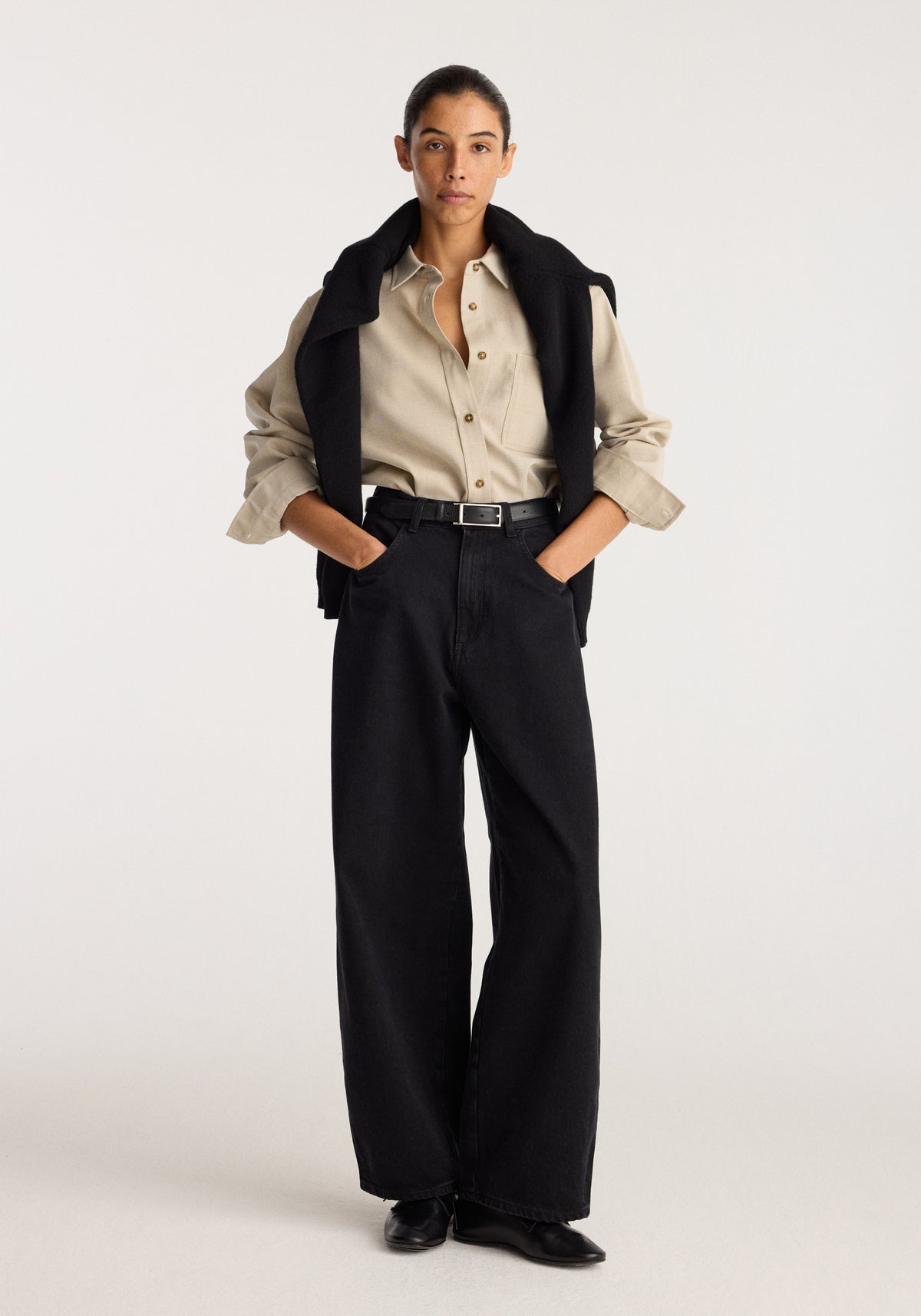 Berber - Barrel leg denim | black worn by a model with a beige shirt and black vest in a full length studio photo