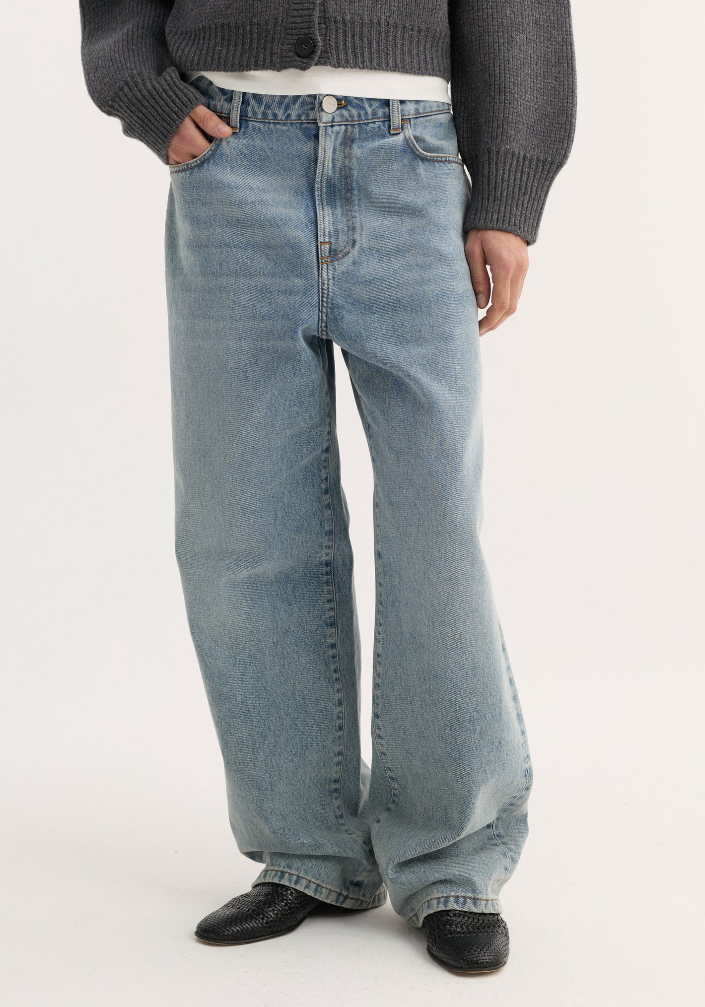 Person wearing Baggy fit denim | classic blue with wide-leg, low-waist design, paired with a dark gray rib-knit sweater and black woven-leather slip-on shoes.