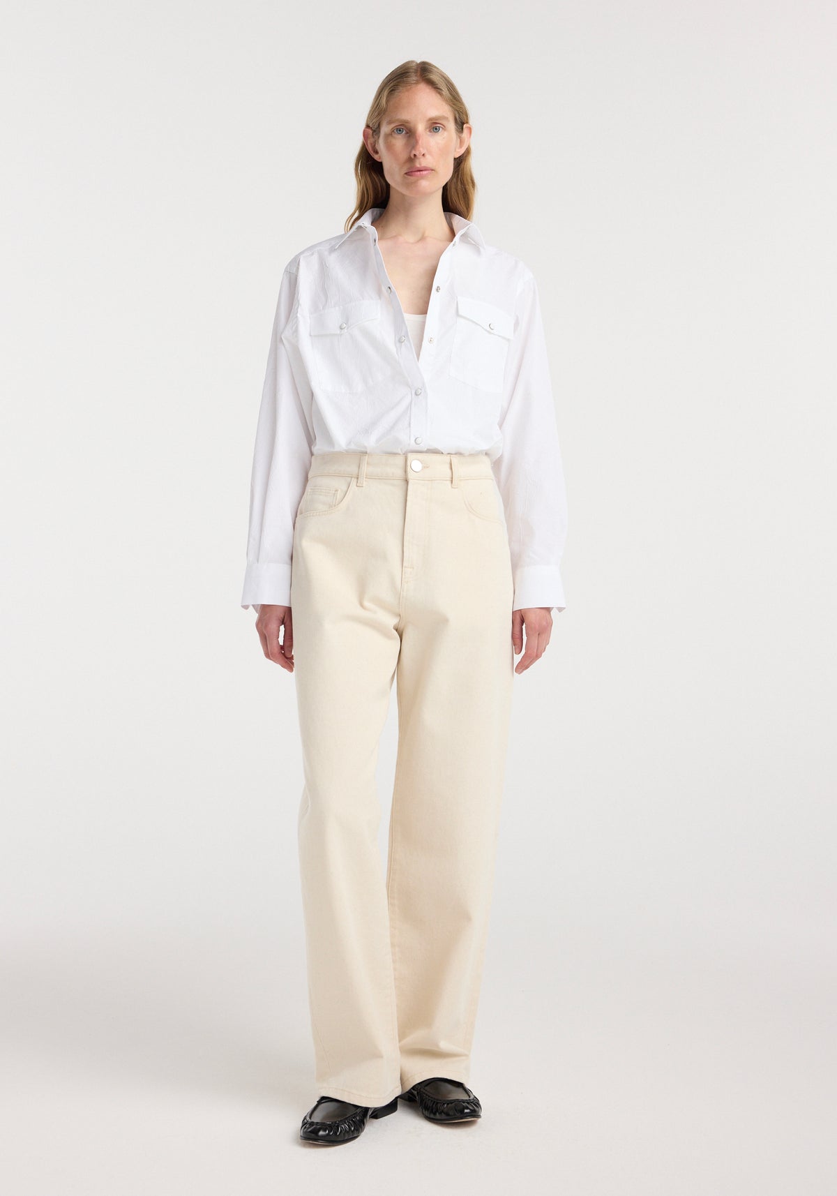 Woman wearing a white button-up shirt and ecru baggy denim jeans standing against a plain white background, showcasing the Bruun - Signature baggy denim | ecru.