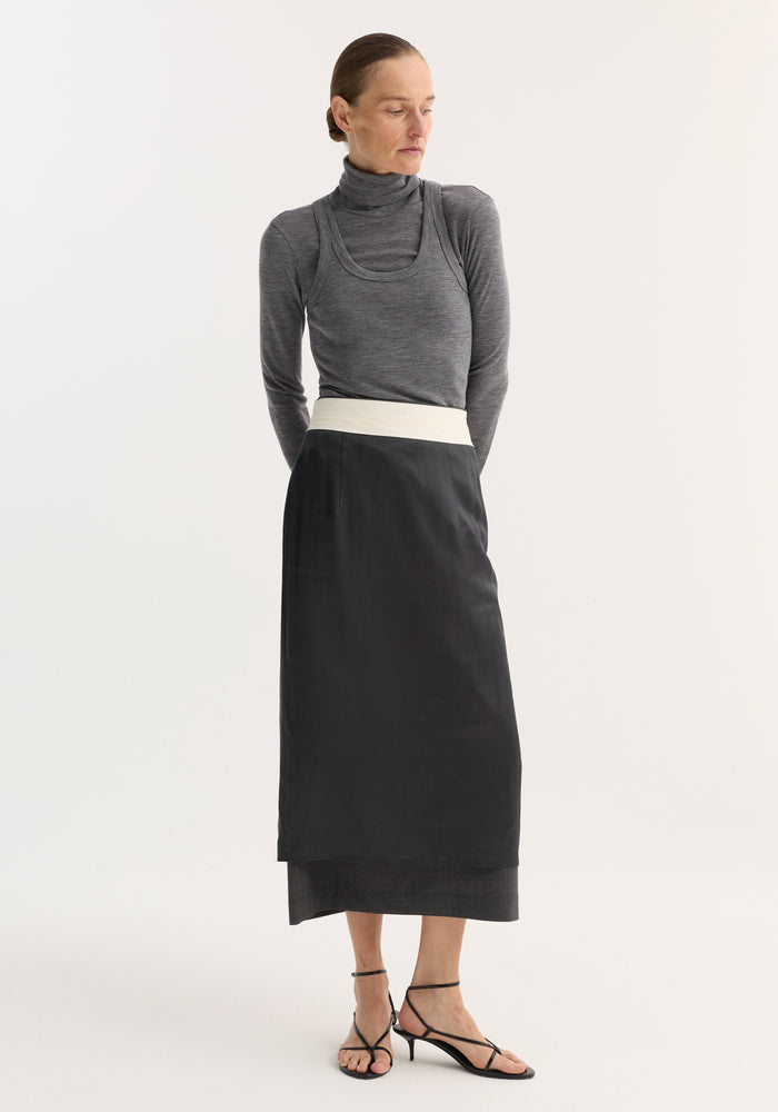 Model in fitted Double-layer wool top, mid grey melange, featuring a turtleneck and tank combo, paired with a high-waisted black skirt and sandals.