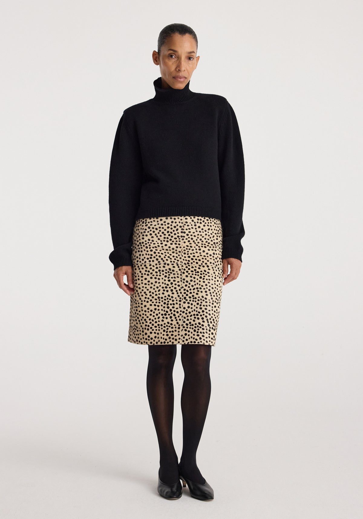 Woman wearing a black turtleneck sweater paired with a Pony hair pencil skirt | cheetah featuring a beige base and black cheetah print, styled with black tights and flats.