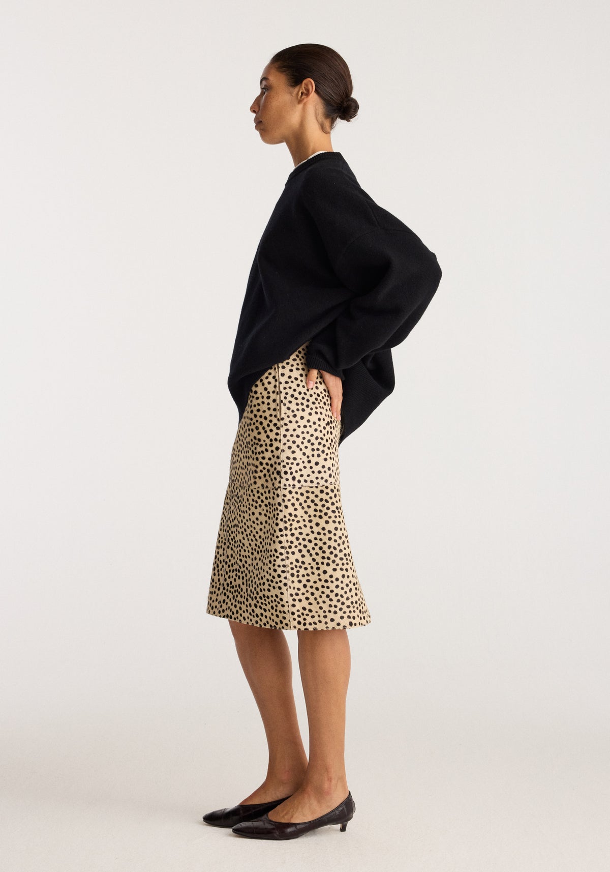 Pony hair pencil skirt | cheetah shown on a model with a black oversized sweater and pointed flats in a studio side view
