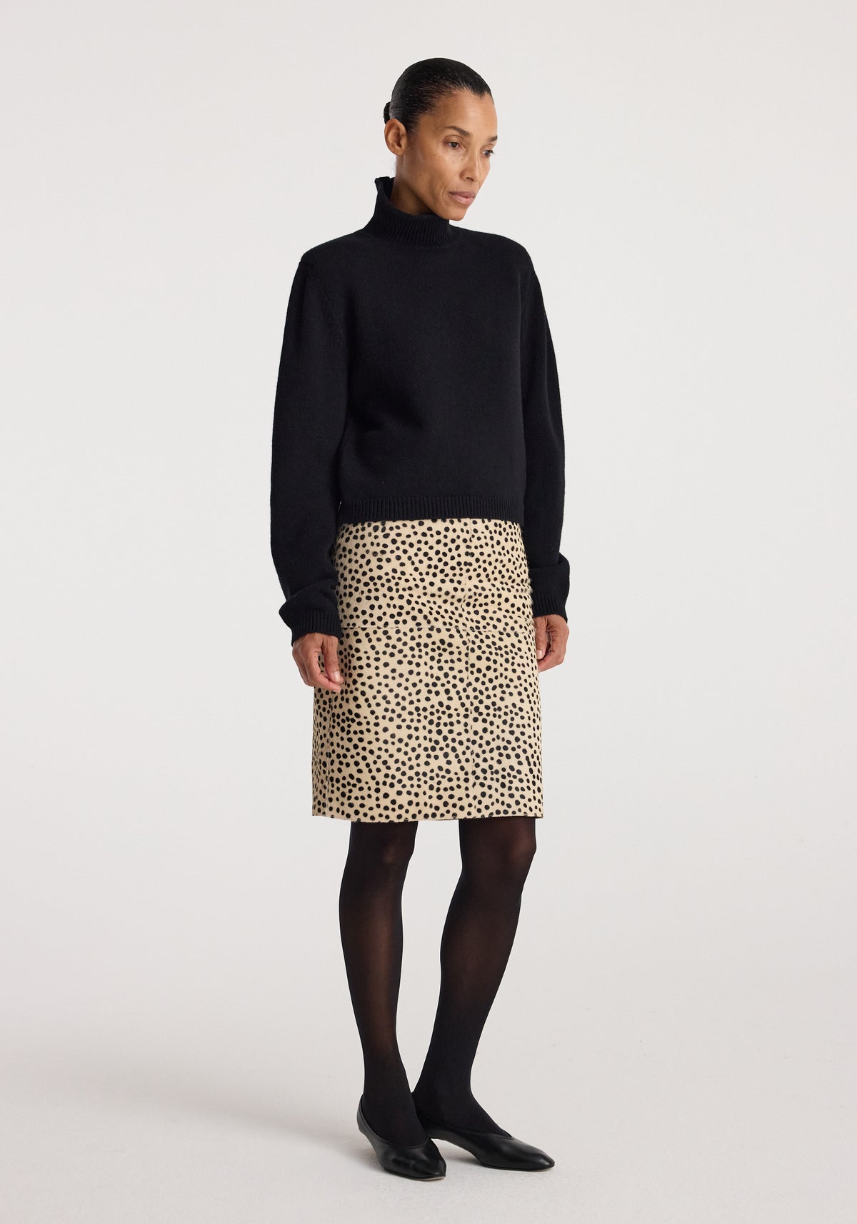 Woman wearing a black turtleneck sweater paired with a Pony hair pencil skirt | cheetah featuring a beige base and black cheetah spots, styled with black tights and flats.