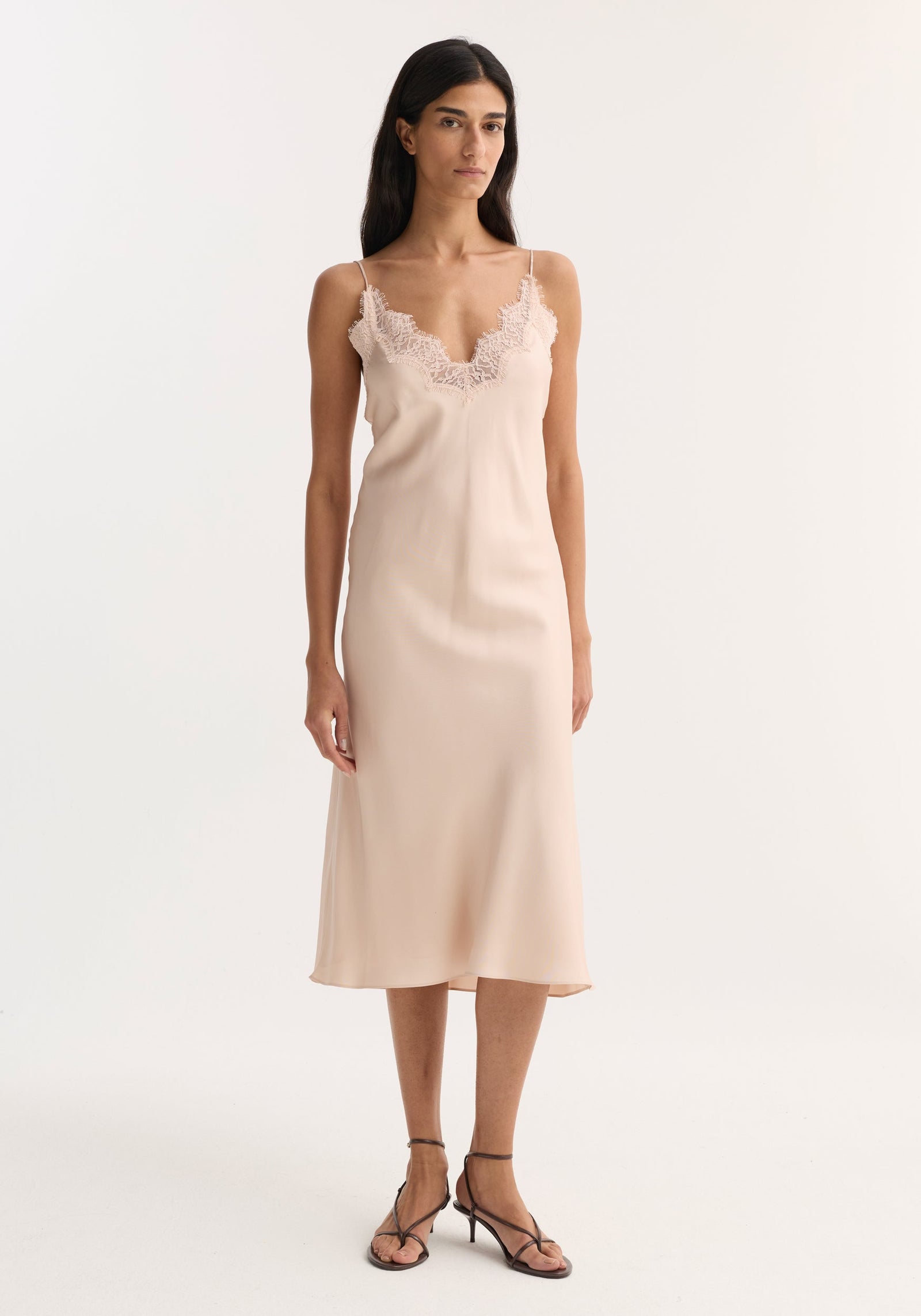A slim woman models the Lace slip dress | rose, a midi silk dress with lace-trimmed neckline and adjustable straps, paired with low-heeled sandals.