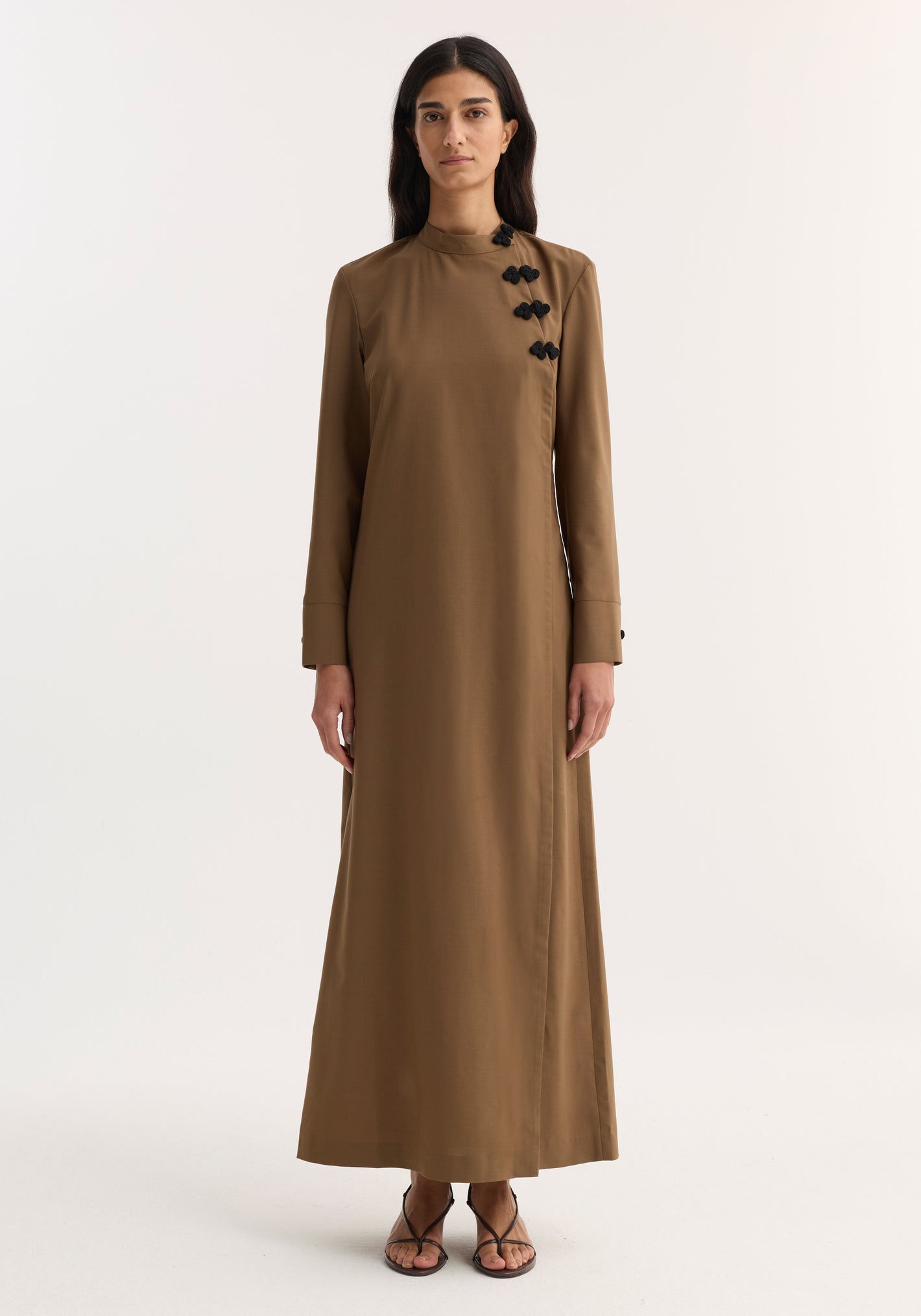 Model wearing Pankou closure dress | mocha, featuring floor-length design, long sleeves, asymmetrical pankou buttons, and side split, paired with black strappy sandals.