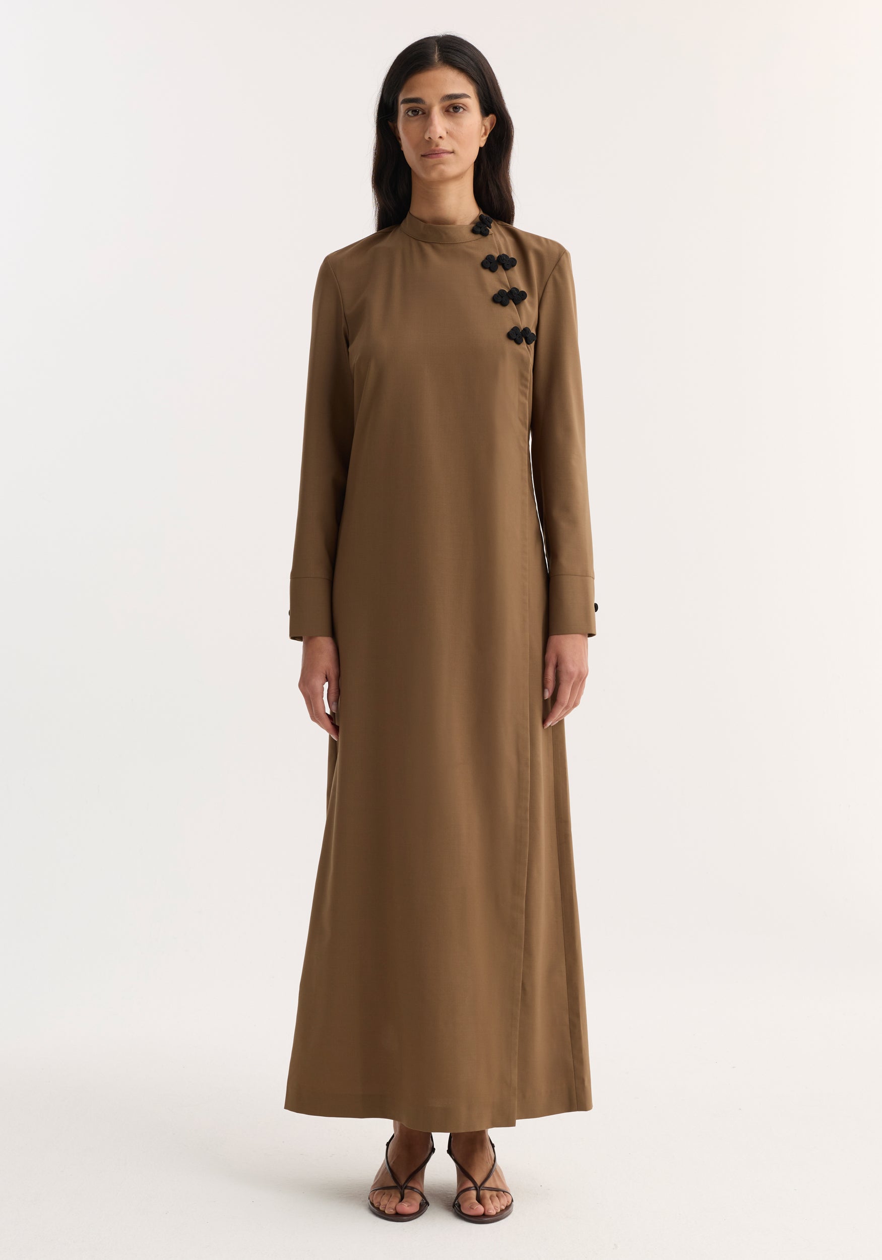 Model wearing Pankou closure dress | mocha, featuring floor-length design, long sleeves, asymmetrical pankou buttons, and side split, paired with black strappy sandals.