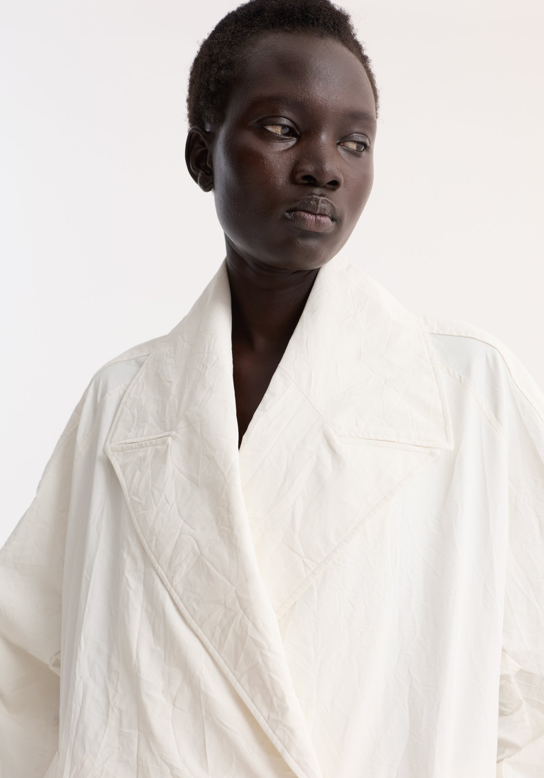 Close-up of a model wearing an oversized crushed cotton coat in off white, featuring a wide collar and textured fabric details.