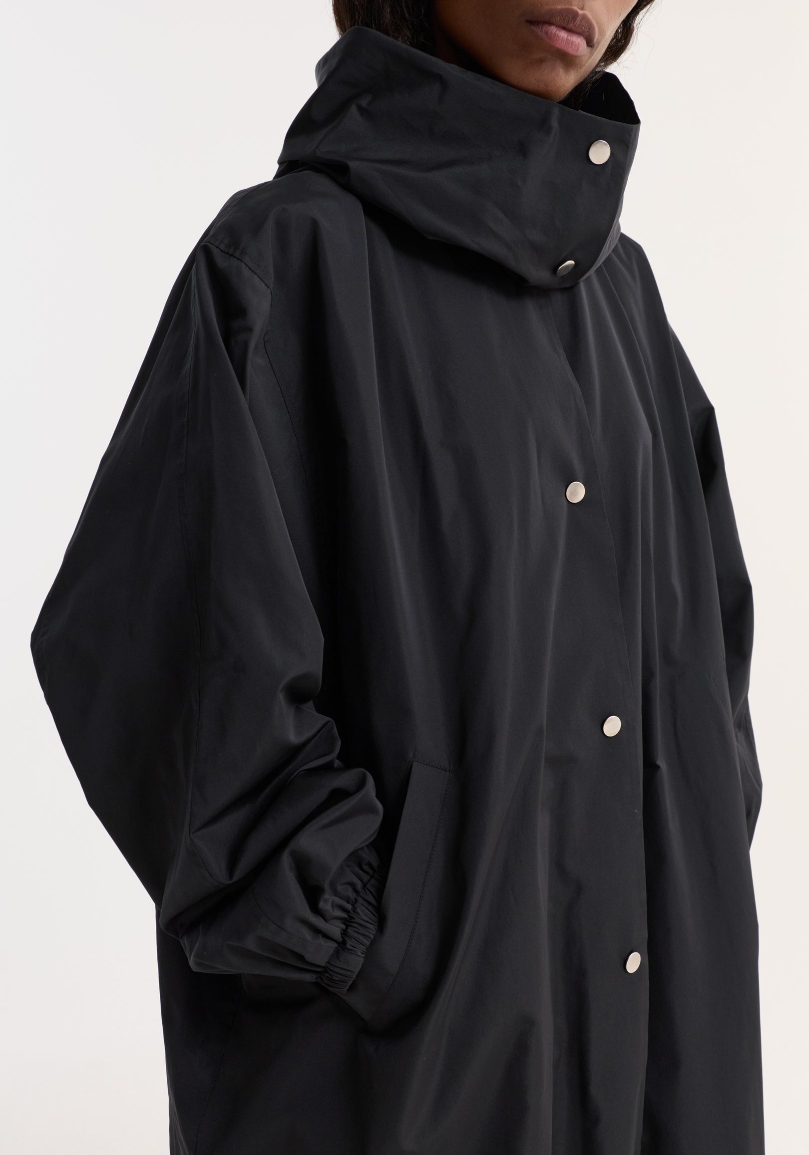 Close-up of a person wearing a black parachute silk-blend coat | black with a high collar, snap button closure, and elasticized cuffs.