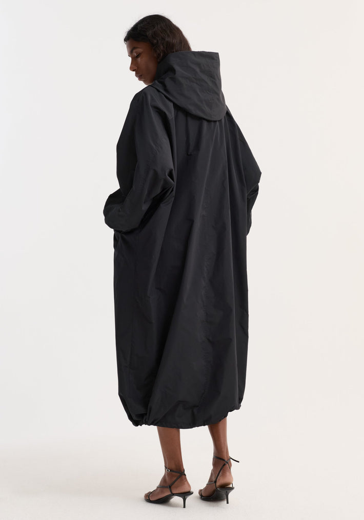 Person in oversized Parachute silk-blend coat | black, with a bubble hem, side pockets, and lightweight crinkled fabric, paired with black strappy sandals.
