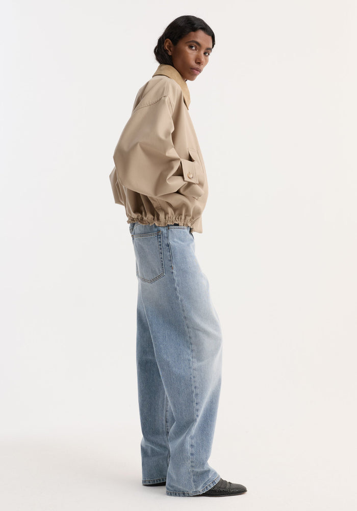Model wearing a suede collar blouson jacket in sand, featuring cropped wide sleeves and a utilitarian design, paired with loose jeans and black slip-ons.
