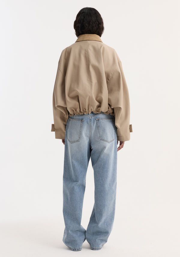 Suede collar blouson jacket in sand with cropped, wide sleeves and elastic hem, paired with high-waisted, relaxed-fit blue jeans on a standing model.