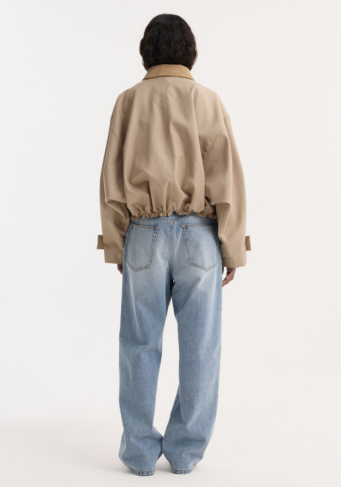 Back view of a person wearing a Suede collar blouson jacket | sand with wide sleeves, suede collar, and gathered hem, paired with wide-leg blue jeans.