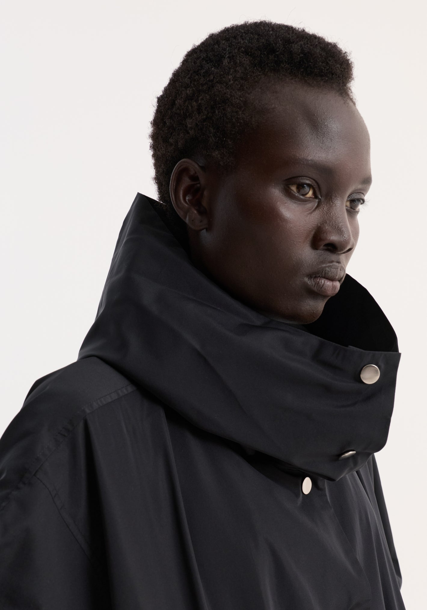 Side-profile of a model wearing the Volume silk-blend jacket in black, featuring a high collar, silver snap buttons, and elasticated cuffs.