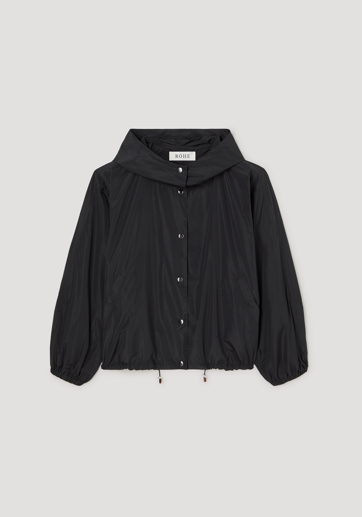 Volume silk-blend jacket in black; oversized with a hood, snap-button front, elastic cuffs, adjustable hem, and angled pockets; brand label RÓHE visible.