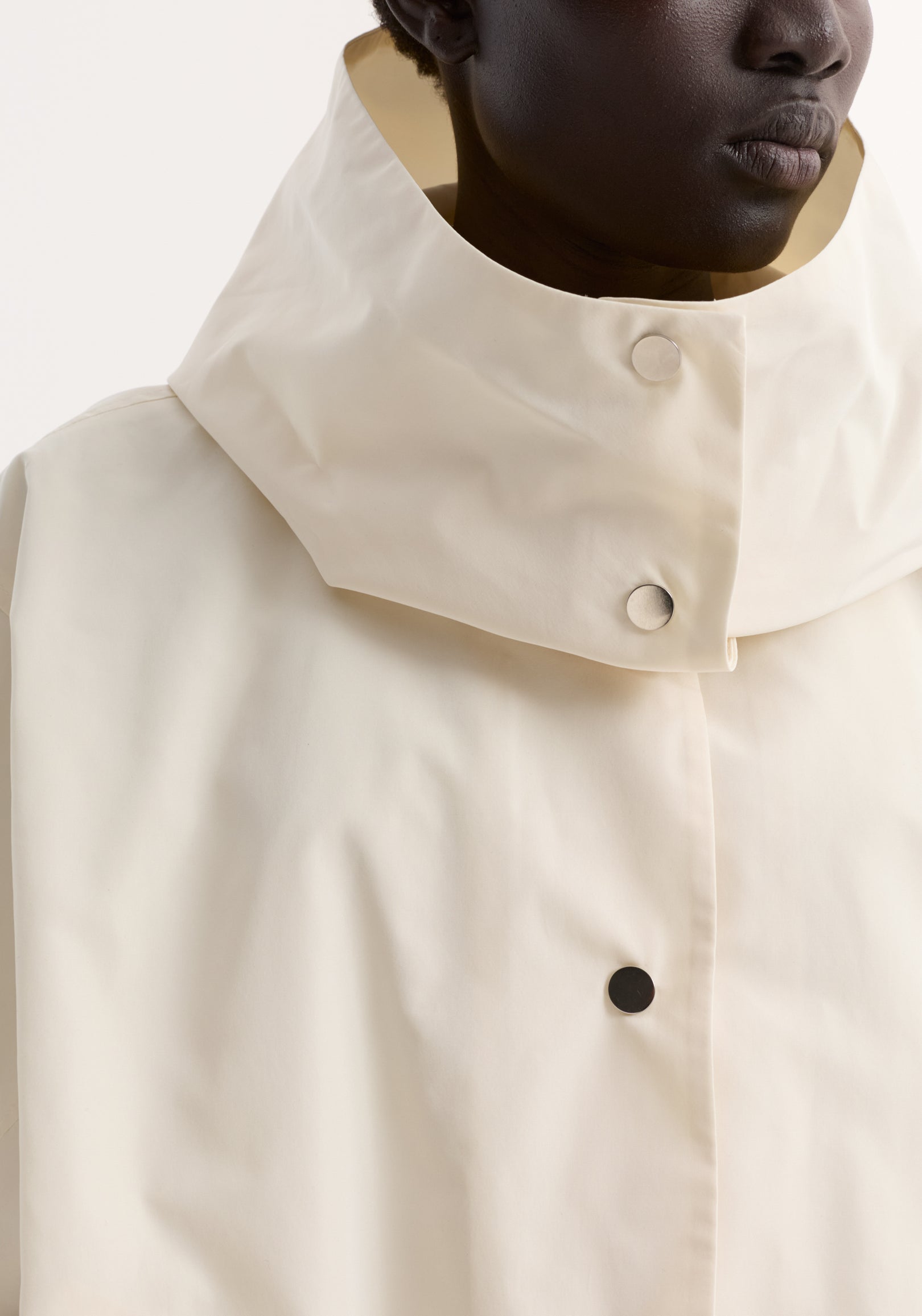 Close-up of a person wearing a cream-colored Volume silk-blend jacket | cream with a high collar and visible snap button closures.