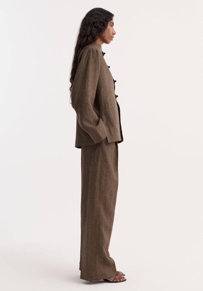 Model in Pankou closure linen jacket with pankou closures and patch pockets, paired with matching trousers and sandals; showcasing the jacket's artisanal design and breathable fabric.