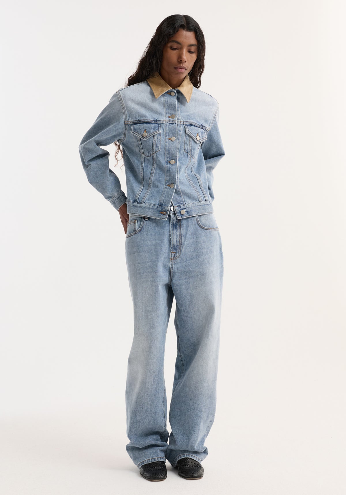 Woman wearing a Suede collar fitted denim jacket | classic blue with light wash denim jeans, standing against a plain background with hands behind her back.