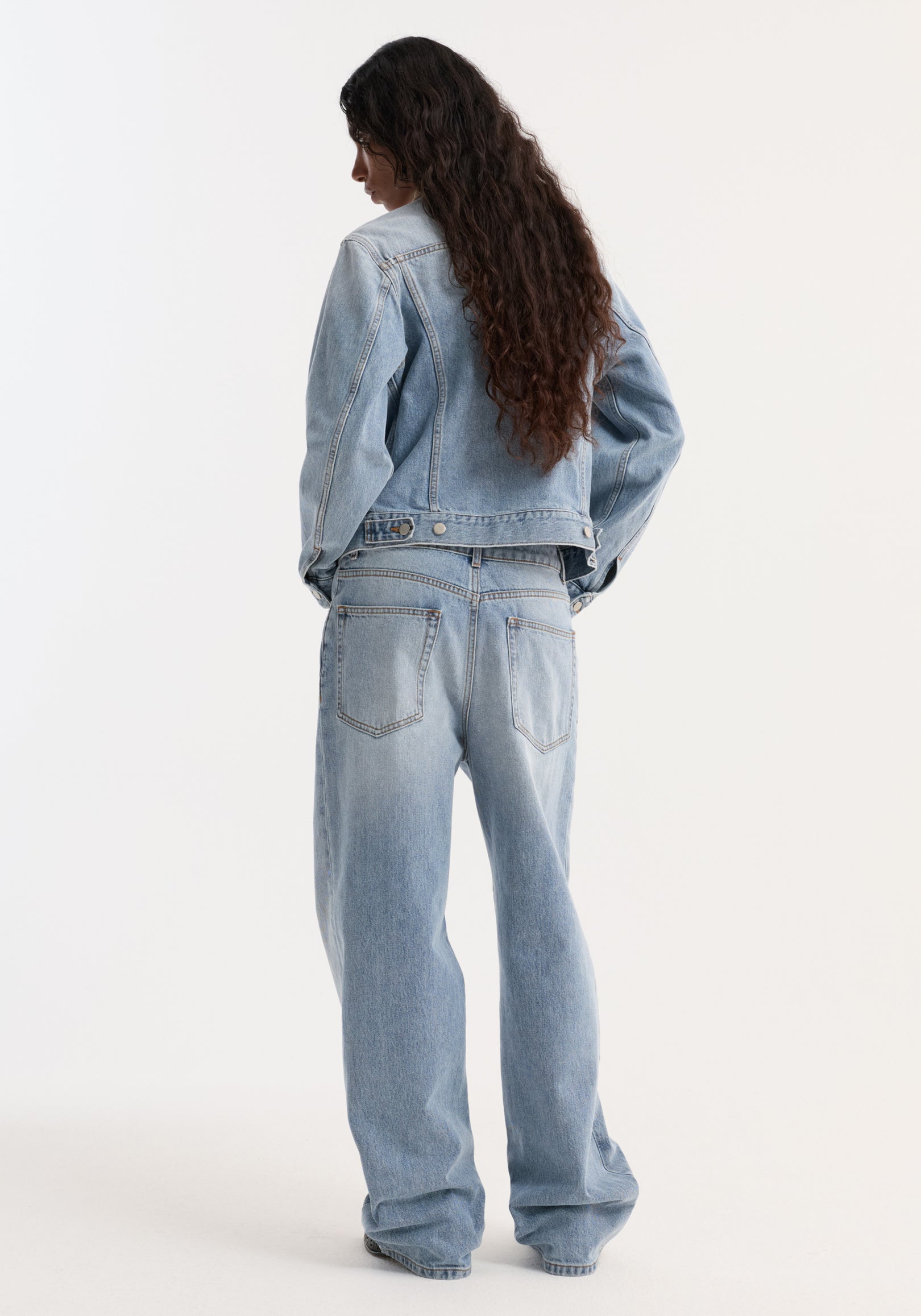 Woman with long dark hair wearing a classic blue Suede collar fitted denim jacket | classic blue, shown from the back paired with matching light blue jeans.