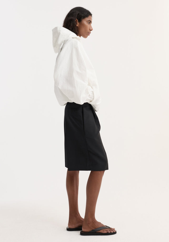 Model wearing a Textured cotton-blend anorak in optic white, featuring a hood, front and side pockets, paired with a tailored black skirt and flip-flops.
