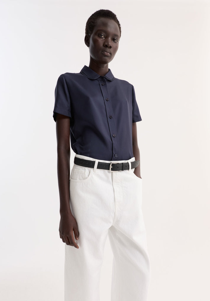 Model in Embroidered Silk Fitted Shirt | Night, showcasing short sleeves, rounded collar, and delicate embroidery, paired with high-waisted wide-leg jeans and a black belt.