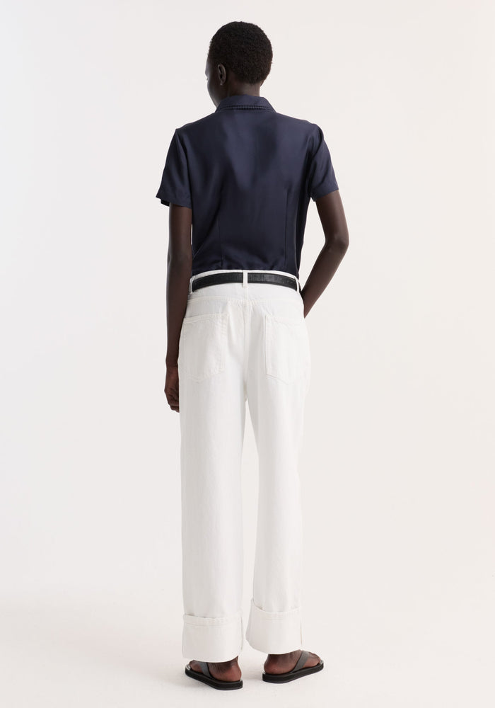 Back view of a person wearing the Embroidered Silk Fitted Shirt in navy, showcasing its classic collar and subtle embroidery, paired with high-waisted white jeans.