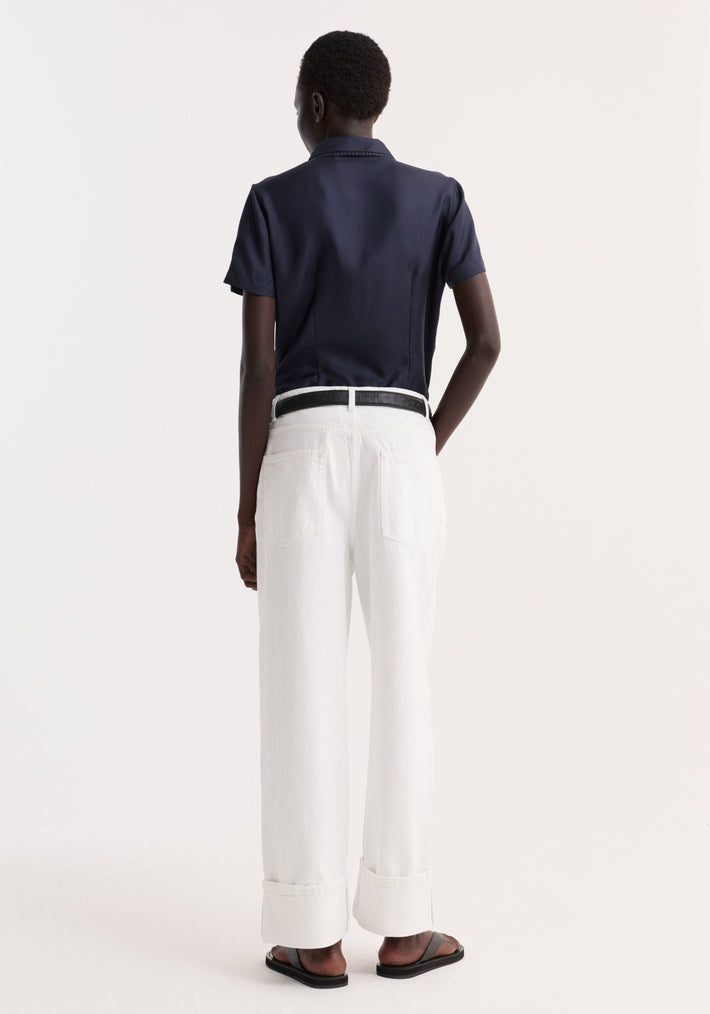 Back view of a person wearing the Embroidered Silk Fitted Shirt in navy, showcasing its classic collar and subtle embroidery, paired with high-waisted white jeans.