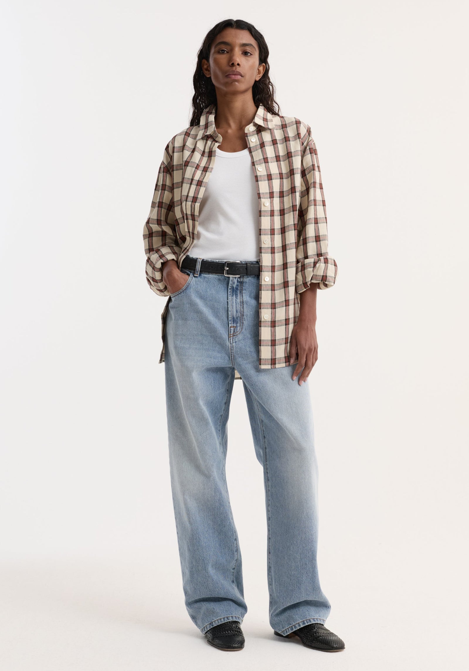 Woman wearing an oversized check shirt in cream, tan, and red tones, styled with loose-fit jeans and slip-on shoes, showcasing a relaxed, effortless look.