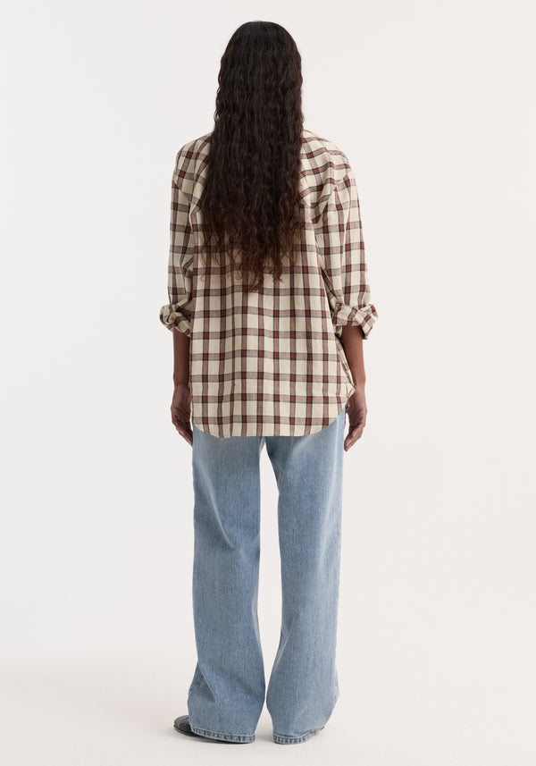 Person wearing an oversized check shirt in red table check pattern, showcasing its relaxed fit with rolled-up sleeves, paired with light-wash jeans.