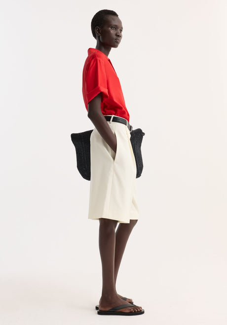 Model wearing Camp collar silk shirt | red, paired with tailored shorts, black belt, sandals, and carrying a slouchy tote. Casual, summery look.