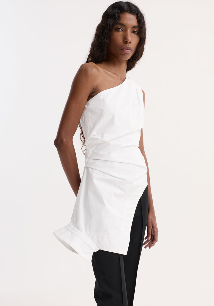 Model wears Reimagined one shoulder top in optic white, showcasing an asymmetrical drape, fitted waist, and deconstructed collar, paired with straight-leg black pants.
