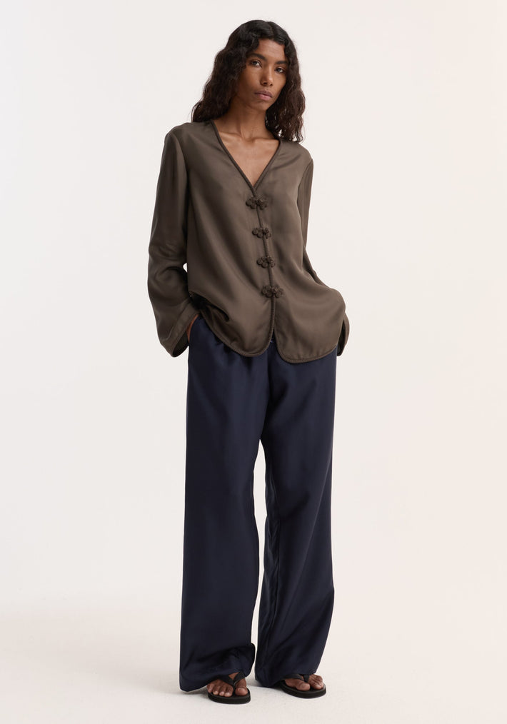 Model wearing a relaxed-fit Pankou closure silk top with decorative frog-style buttons and embroidered edges, paired with high-waisted wide-leg trousers and black sandals.