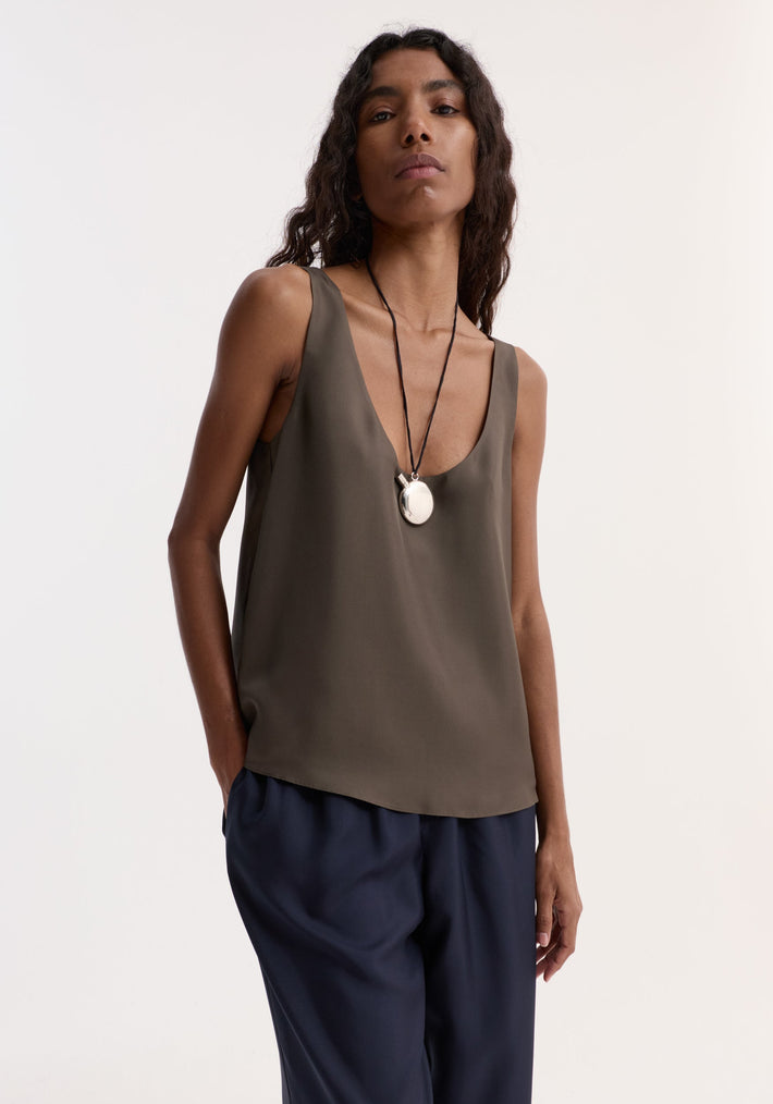 Person wearing the Silk scoop-neck top, showcasing its loose fit and fluid drape, tucked into wide-leg trousers, with a silver pendant necklace.