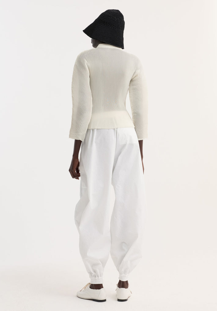 Dark-skinned figure wears a Plissé cardigan with stand-up collar, fabric-covered buttons, and patch pockets, styled over high-waisted trousers and lace-up shoes.