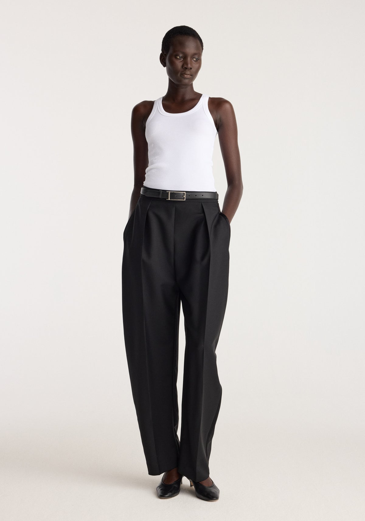 Scoop knitted top | optic white worn by a model with black pleated trousers and loafers in a neutral studio setting