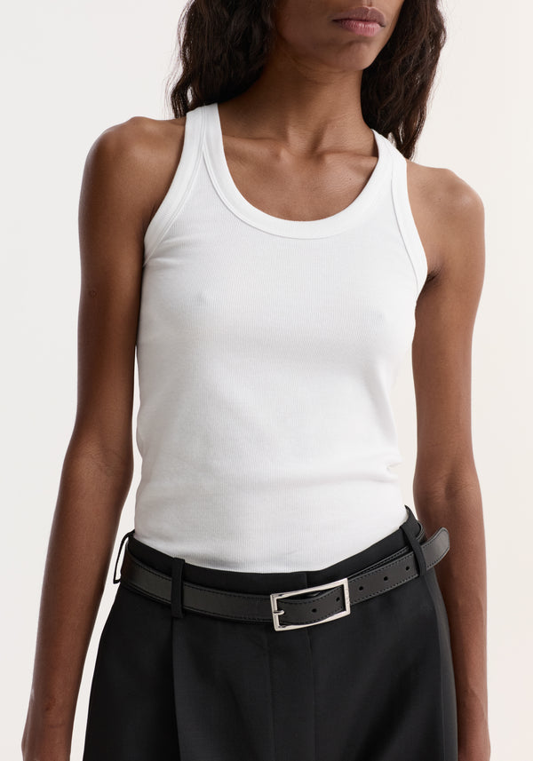 Person wearing the Scoop-neck rib top in optic white, showcasing its scoop neck and racerback design, paired with black trousers and a leather belt.