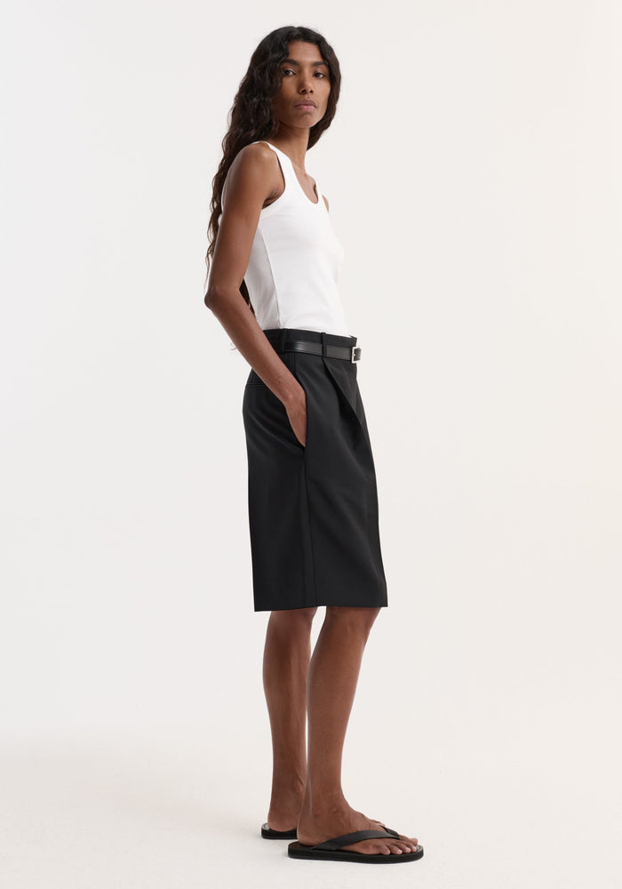 Model in profile wearing a Scoop-neck rib top in optic white with a racerback, paired with high-waisted tailored shorts and flip-flops.