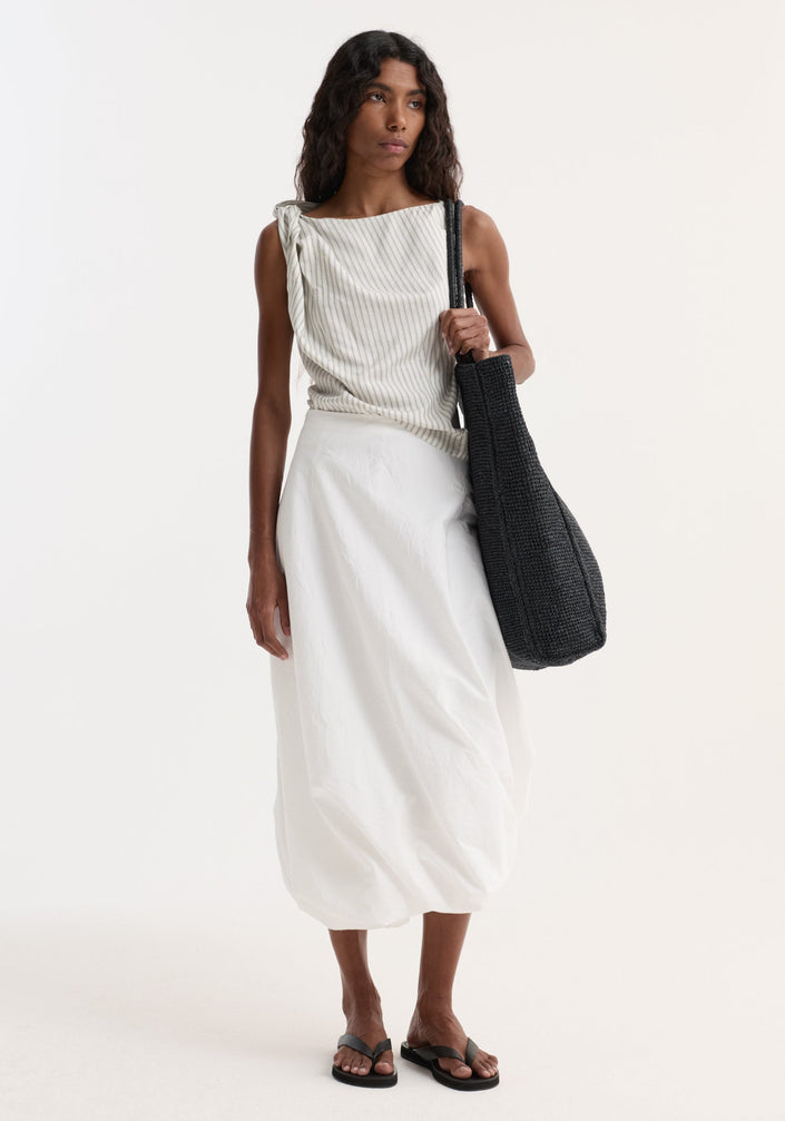 Model wearing a Silk-blend draped top | fine stripe with a one-shoulder twist and asymmetrical silhouette, paired with a mid-calf bubble skirt and black slide sandals.