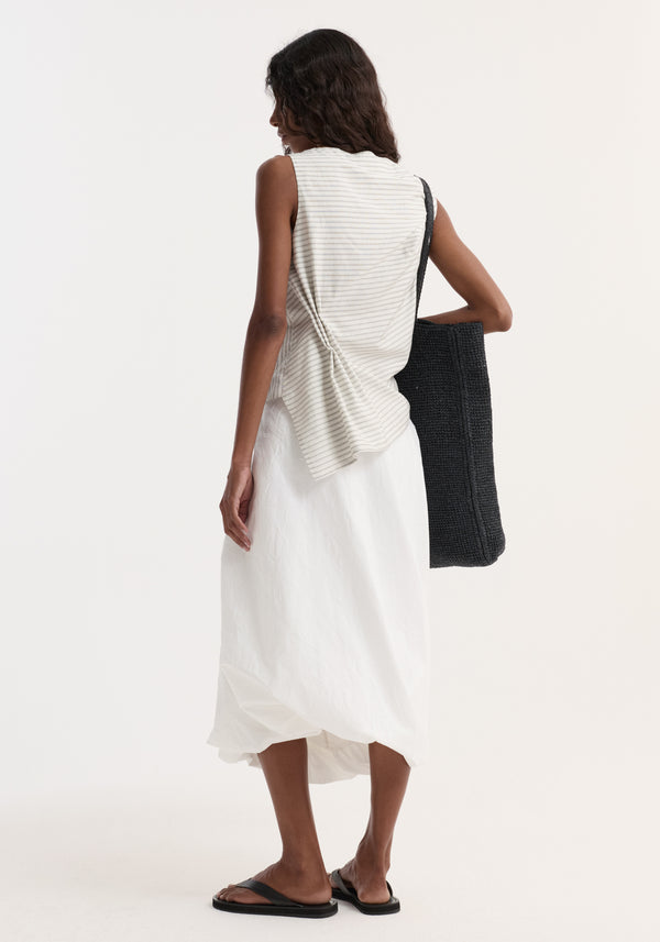 Woman in a sleeveless Silk-blend draped top with a twist detail, boat neck, and asymmetrical silhouette, paired with a mid-calf skirt and black tote.