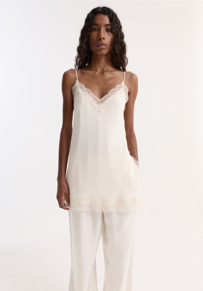 Model wearing Lace camisole | off white with lace-trimmed V-neck, adjustable straps, wide-leg trousers, and black sandals, highlighting a fluid, elegant silhouette.