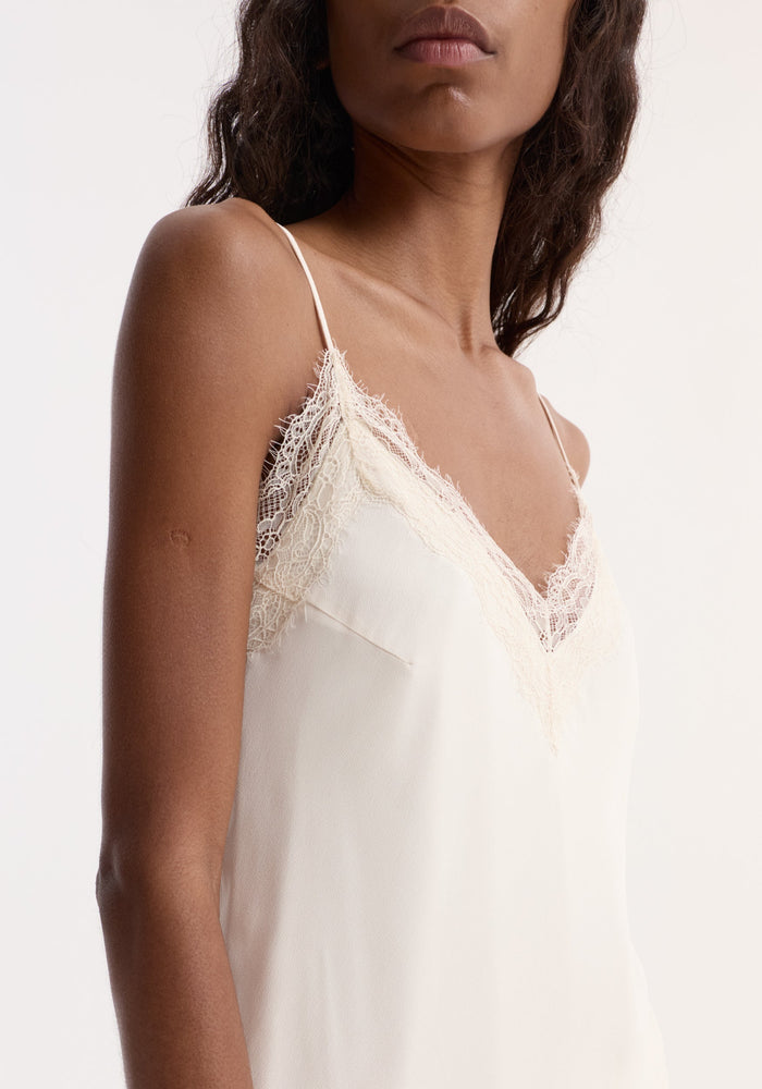 Lace camisole | off white features a cream-colored, silky top with lace-trimmed V-neckline and thin straps, highlighting an elegant, fluid silhouette.